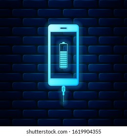 Glowing neon Smartphone battery charge icon isolated on brick wall background. Phone with a low battery charge and with USB connection.  Vector Illustration