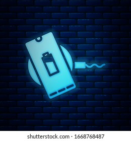 Glowing neon Smartphone charging on wireless charger icon isolated on brick wall background. Charging battery on charging pad.  Vector Illustration