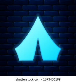 Glowing neon Tourist tent icon isolated on brick wall background. Camping symbol.  Vector Illustration