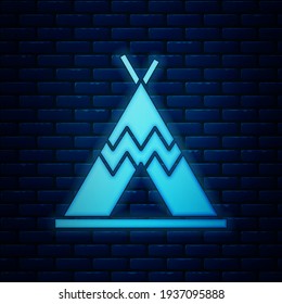 Glowing neon Traditional indian teepee or wigwam icon isolated on brick wall background. Indian tent.  Vector