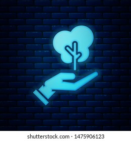 Glowing neon Tree in hand of environmental protection icon isolated on brick wall background. Seed and seedling. Planting sapling. Ecology concept.  Vector Illustration