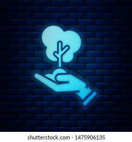 Glowing neon Tree in hand of environmental protection icon isolated on brick wall background. Seed and seedling. Planting sapling. Ecology concept.  Vector Illustration