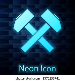 Glowing neon Two crossed hammers icon isolated on brick wall background. Tool for repair. Vector Illustration