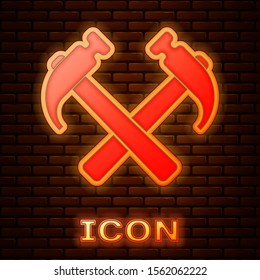 Glowing neon Two crossed hammers icon isolated on brick wall background. Tool for repair.  Vector Illustration