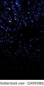 Glowing particles, polka dots on a dark blue background. Vertical festive banner. An elegant holiday pattern. Vector illustration.