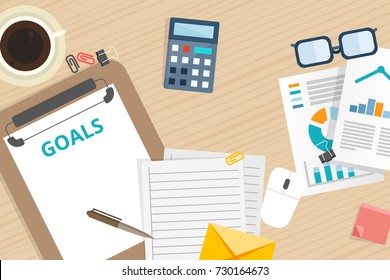 "Goals" text on paper sheet with chart, spectacles, pen, and paper clip on wooden table