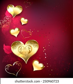 Gold, jewelry hearts on red textural background with leaves of roses.