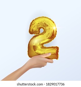 Gold number two 2 metal ball. Party decoration with Golden balloons. The number 2 in your hand.Anniversary sign for a happy holiday, celebration, birthday, New year. The design of the metal balloon.