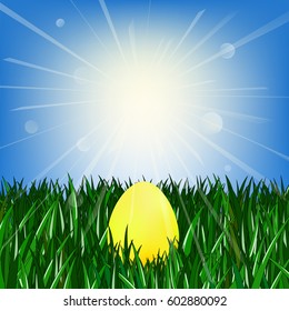 Golden egg on the green grass against the blue sky with the sun