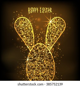 Golden floral design decorated Easter Egg with Bunny Ears on shiny brown background.