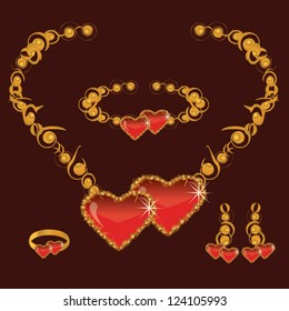 golden set from necklace ring earrings and bracelet with heart from red stone on dark background