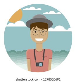 Good smiling young bespectacled guy in a gray hat on the beach. Tropical landscape on the background. Tan on the face and hands. Camera. The man is a European tourist. Sea, hot sun, clouds, blue sky