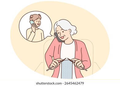 Grandmother makes phone call to granddaughter and knits scarf sitting in chair. Elderly woman with phone is talking to granddaughter, asking how things are at school or inviting to come visit