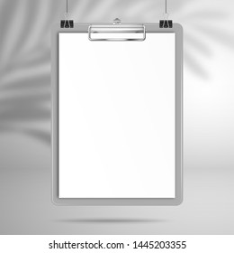 Gray clipboard with a blank white sheet of paper hang on clips above the surface. The shadow of the palm tree leaf falls on the wall behind. Mockup for design