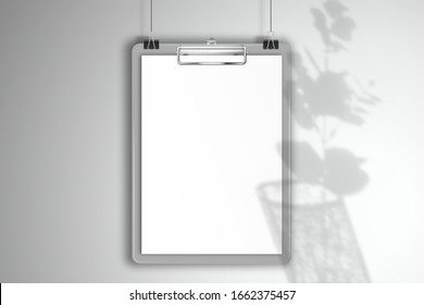 Gray clipboard with a blank white sheet of paper hang on clips. Mockup for design with shadow of a eucalyptus branch in an openwork glass