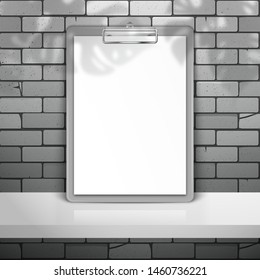 Gray clipboard with white blank paper stands near the brick wall on the shelf. The shadow of the leaves of the Monstera plant is on top. Mockup for design