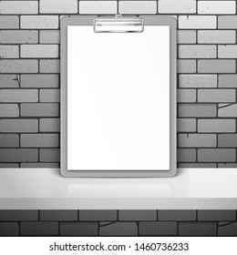 Gray clipboard with white blank paper stands near the brick wall on the shelf. Mockup for design with shadow