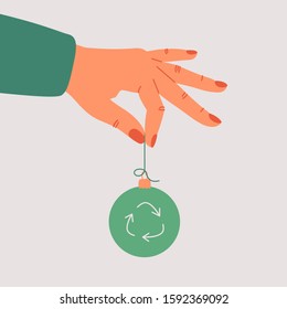 Green Christmas concept. Vector eco-friendly sustainable illustration.  The human hand holds a green Xmas toy with a recycling symbol.