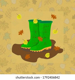 green muddy rubber boots in a muddy puddle with falling oak and linden leaves