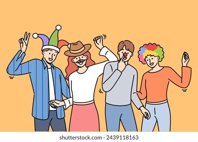 Group of friends participating in masquerade with funny hats or fake mustaches, dancing and enjoying festive party. Young men and women enjoy relaxing together at student party after end of session.