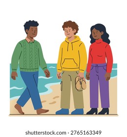 A group of three young adults, two men and one woman, stand on a sandy beach with the ocean in the background. They are casually dressed and appear to be conversing.