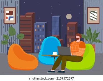 Guy with computer on background of night city view. Freelance, internet work, remote job concept. Man sitting with laptop and working online. Freelancer working from home with cityscape in window