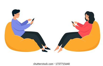 A guy and a girl are sitting on a bean bag chair and holding a smartphone in their hands. Happy young people communicate on the Internet. 