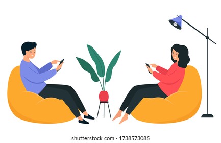 A guy and a girl are sitting on a bean bag chair and holding a smartphone in their hands. Happy young people communicate on the Internet. 