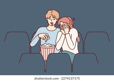 Un hombre y una chica están viendo una película de terror en el cine y comiendo palomitas de maíz disfrutando de películas sobre vampiros. Mujer temerosa cierra los ojos con las manos sentadas en el cine cerca de un hombre viendo una película de terror con interés 