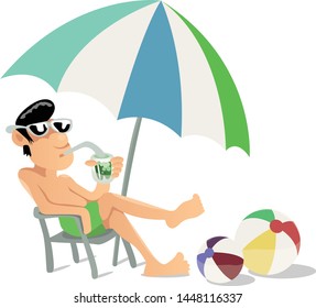 Guy in green shorts sunbathing on a beach under umbrella and drinking cold green juice.