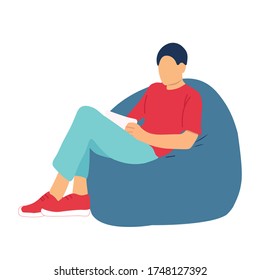 A guy with a laptop or tablet, a book, sitting on a chair or ottoman in his living room. Freelance or learning concept. A man chatting with friends or chatting with work colleagues or reading a story