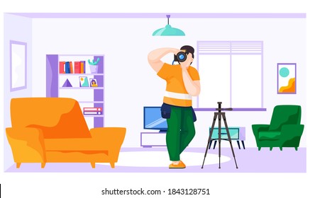 The guy is a photographer holding a camera in his hands and takes pictures. Photographing in the apartment. Photo making process. The man looks at the viewer and adjusts the lens. Shooting in the flat