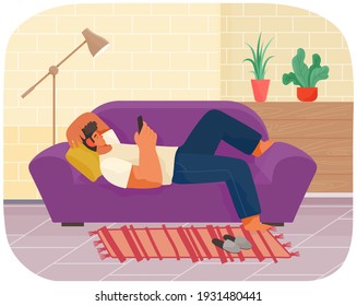 Guy playing on smartphone is lying on violet couch. Man relaxing at home alone. Living room interior design and furniture arrangement in apartment. Person with phone lies and looks at screen