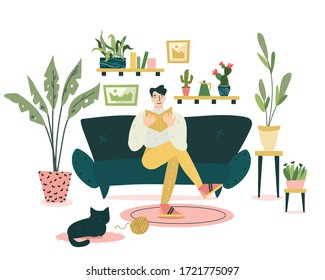 Guy is sitting on the coach and reading an interesting book in cozy and nice living room. Black cat is sleeping on the carpet around him. A lot of different plants on the background.