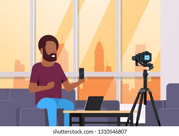 guy technology blogger recording video on camera. african man showing new smartphone functional testing blog concept modern apartment interior closeup horizontal