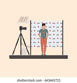 Guy vloglogger in a T-shirt, sneakers in front of the camera on a tripod. Behind the back seamless pattern flat filming