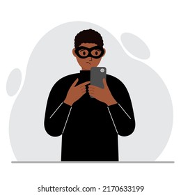 Hacker con una máscara negra con un teléfono móvil. El cibercriminal sostiene un smartphone. Ciberataque, phishing móvil, estafa. Ilustración plana del vector