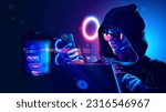 Hacker or phone scammer in hood hacking at computer and mobile smartphone in dark room. Computer criminal uses malware on phone to hack devices. Hacker in dark hoodie in room with neon light using pc