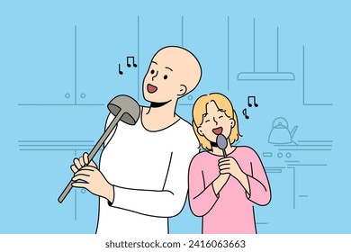 Hairless boy and little girl sing standing in kitchen, use utensils instead microphone, imagine visit in karaoke. Sister supports brother dreams of going to karaoke after undergoing cancer treatment