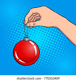 Hand with christmas tree toy pop art retro vector illustration. Comic book style imitation.