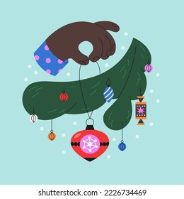 Mano decora una rama de un árbol de Navidad y nieve en un fondo azul claro. Cuidada tarjeta de bienvenida colorida.