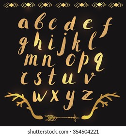Hand drawn alphabet letters written with brush pen. Handwritten font are decorated with ornamental boho tribal style elements. Modern calligraphy letters in gold over black background