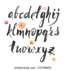 Hand drawn alphabet written with brush pen. Letters are decorated with watercolor flowers. 