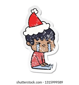 hand drawn distressed sticker cartoon of a boy crying wearing santa hat