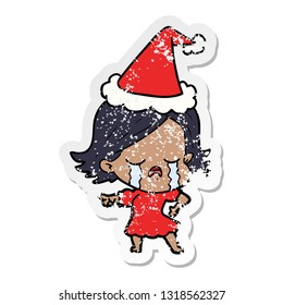 hand drawn distressed sticker cartoon of a girl crying and pointing wearing santa hat