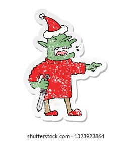 hand drawn distressed sticker cartoon of a goblin with knife wearing santa hat