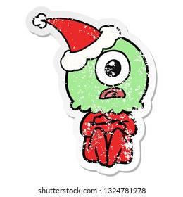 hand drawn distressed sticker cartoon of a cyclops alien spaceman wearing santa hat