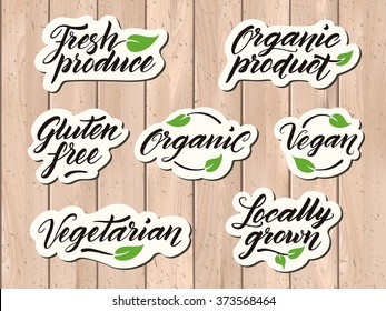 Hand drawn healthy food letterings. Label, badge, logo template on a wooden background. Organic, organic product, gluten free, vegan, locally grown, vegetarian, fresh produce. Eps 10 vector.