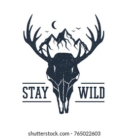 Hand drawn inspirational label with mountains and deer skull textured vector illustrations and "Stay wild" lettering.