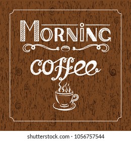 Hand drawn lettering "Morning coffee" with charcoal effect and view of a cup of coffee on brown wood background.